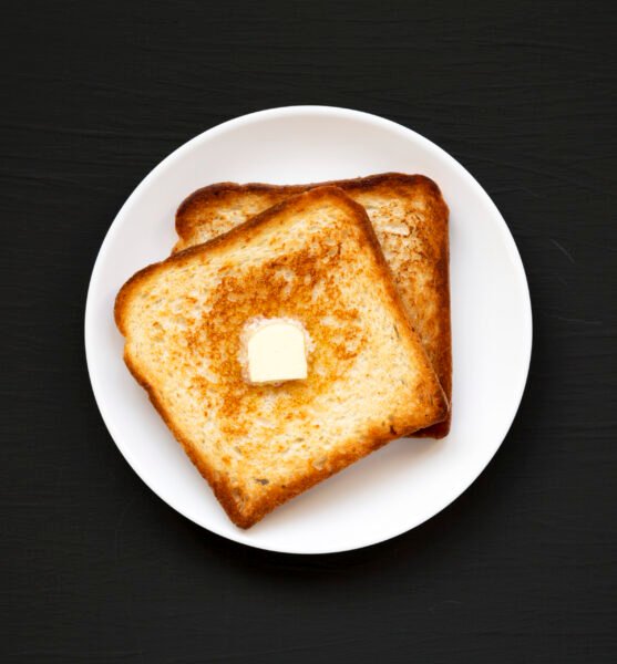 Homemade Buttered Toast on a white plate on a black surface, top view. Flat lay, overhead, from above.