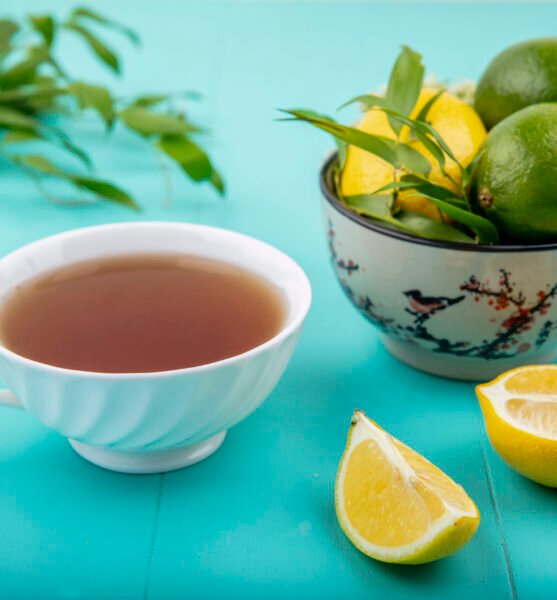 side view of lemons on a bowl with a cup of tea slices of lemon on blue background