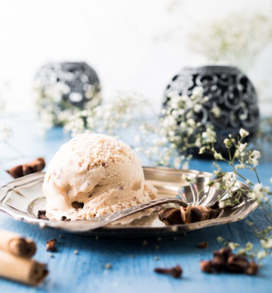 Scoop of homemade ice cream with cinnamon, apple syrup and spices on metal plate on blue wooden background. Summer food concept.