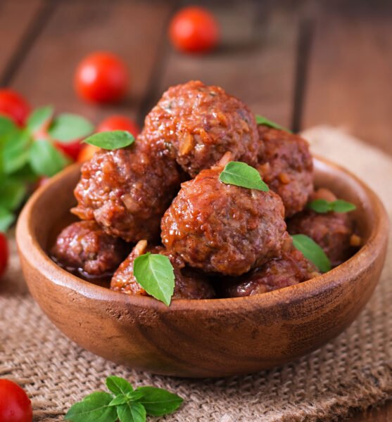 Meatballs in sweet and sour tomato sauce and basil in a wooden bowl